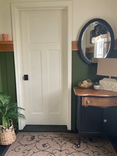 Entry with deep green wainscoting, a black antique dresser, and a round mirror