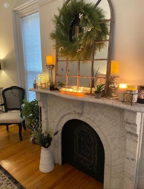 Marble fireplace mantel styled with candles, greenery, and an arched mirror