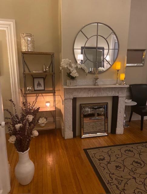 Parlor corner with a marble mantel, round window mirror, orchids, and candlelight
